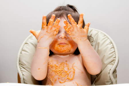Baby spreading spaghetti over face, hands, and chest