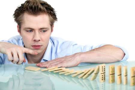 man toppling stacked dominos signifying long-term impacts of actions