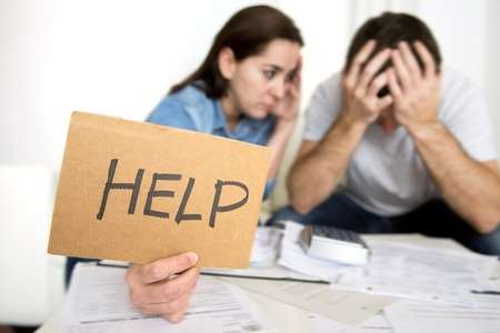 Couple holding help sign while looking at bills