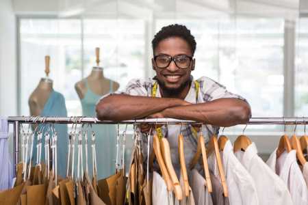 self-employed tailor posing over rack of shirts